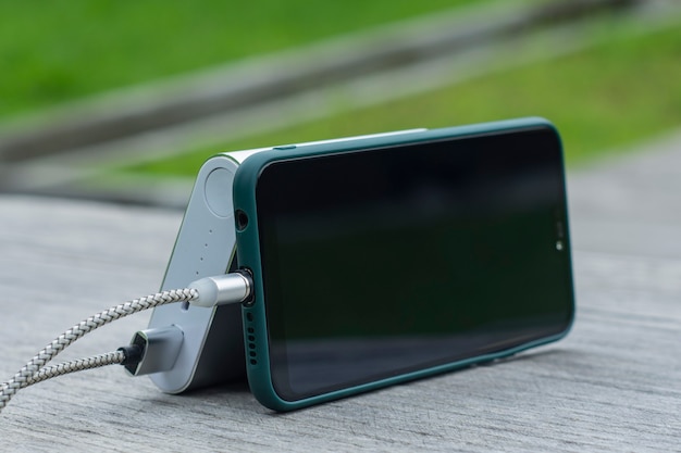 Photo power bank charges a smartphone on a wooden bench in the park.