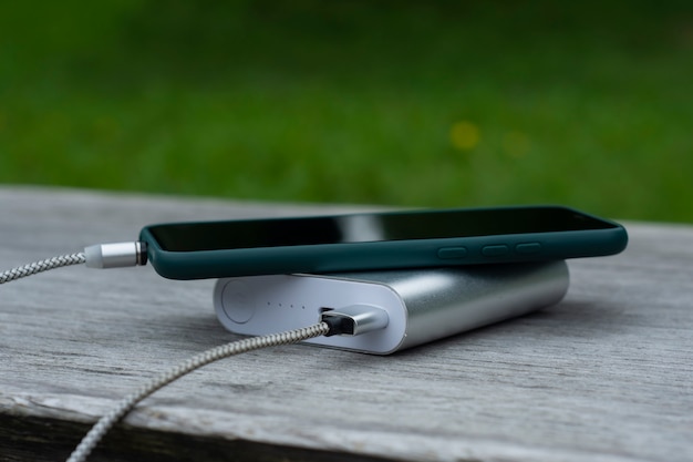 Power Bank laadt een smartphone op een houten bankje in het park.