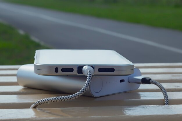 Foto power bank laadt een smartphone op een houten bankje in het park.