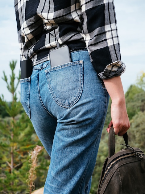 Power Bank и смартфон лежат в задних карманах джинсов девушки.