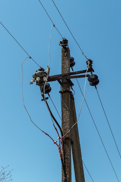 Power line post met elektriciteitskabels tegen een heldere hemel met witte wolken