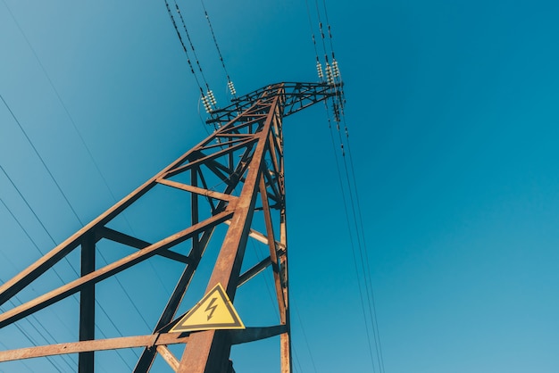 Power lines on background of blue sky close-up. Electric hub on pole. Electricity equipment with copyspace. Wires of high voltage in sky. Electricity industry. Tower with lightning warning sign.