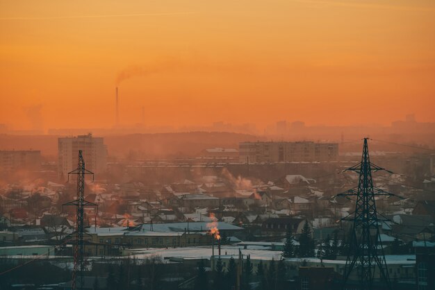 Линии электропередач в городе на рассвете. Силуэты городских зданий среди смога на восходе солнца.