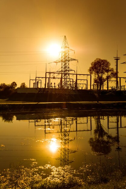 Power lines and substation on the background of bright yellow sunset on the riverbank
