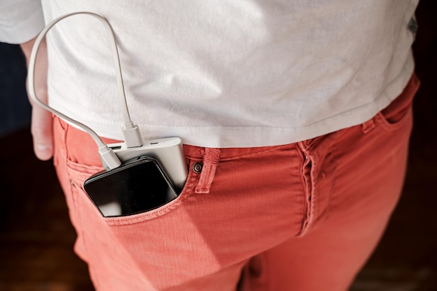 Powerbank en een mobiele telefoon die wordt opgeladen, ligt in het voorvak van een koraalkleurige spijkerbroek