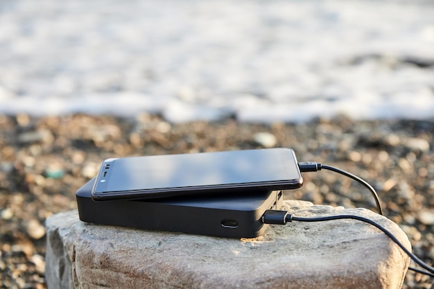 Powerbank laadt de telefoon op op het strand aan zee