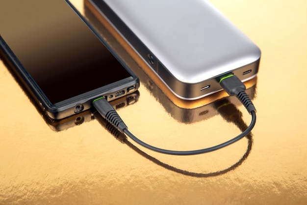 Powerbank laadt een smartphone op een gouden achtergrond Elektronische apparaten voor het opladen van gadgets en smartphones