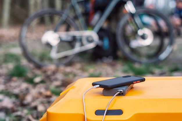 Powerbank laadt een smartphone op een toeristische koelkast tegen de achtergrond van een fiets in de natuur Concept over het thema toerisme en reizen