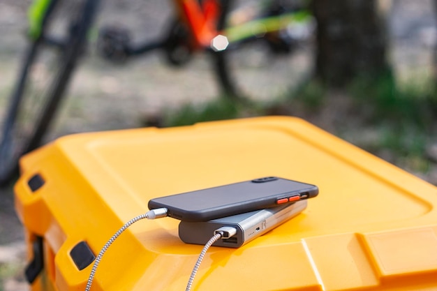 Powerbank laadt een smartphone op een toeristische koelkast tegen de achtergrond van een fiets in de natuur Concept over het thema toerisme en reizen