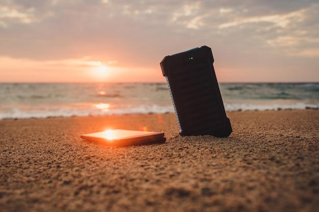 Powerbank nella sabbia sullo sfondo del sol levante nel cielo nuvoloso e nel mare blu. fonte di energia alternativa. la batteria è caricata dall'energia solare. ricaricare i dispositivi mobili in libertà. isola.