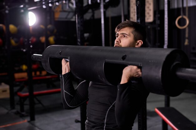 Powerful athlete raising weights up, using sportive equipment in moder gym, man is concentrated on sport training workout. handsome guy in sportive outfit