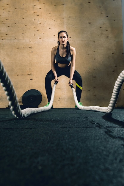 Powerful attractive muscular woman CrossFit trainer do battle workout with ropes