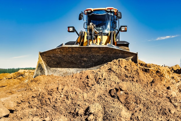 Powerful bulldozer or loader moves the earth at the construction site against the sky An earthmoving machine is leveling the site Construction heavy equipment for earthworks