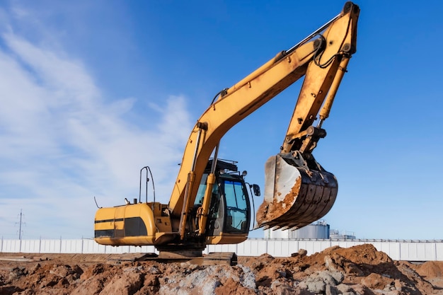 Un potente escavatore a cingoli scava il terreno contro il cielo blu lavori di sterro con attrezzature pesanti in cantiere