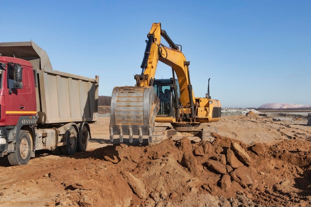 A powerful crawler excavator loads the earth into a dump truck against the blue sky Development and removal of soil from the construction site