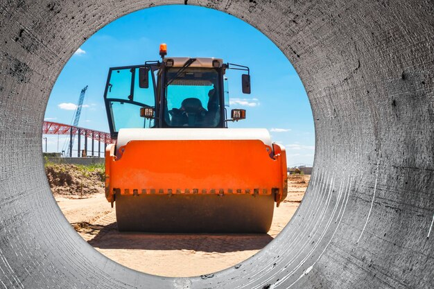 Rullo pesante e potente con cabina chiusa contro un cielo nuvoloso blu la pista di pattinaggio prepara il terreno per la costruzione di una nuova strada attrezzature per l'edilizia stradale