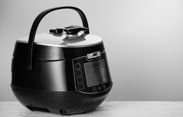 Powerful modern multicooker on white wooden table.