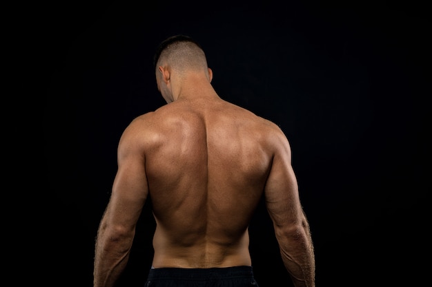 Photo powerful muscular athlete shows off his back beside black wall