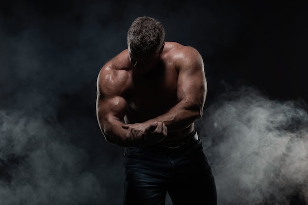 Powerful muscular man shows biceps on black. Strength and fitness concept