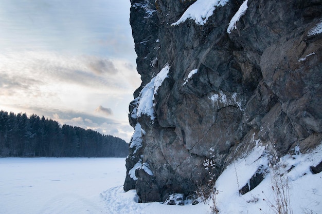 Powerful rocks covered with snow on the banks of a frozen river. Weather, climate.