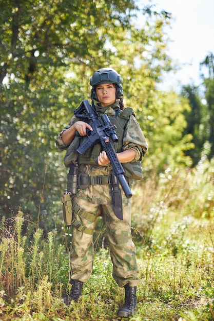 Powerful sportive woman soldier ready for battle wearing protective military gear weapon, rifle or gun. in wild nature