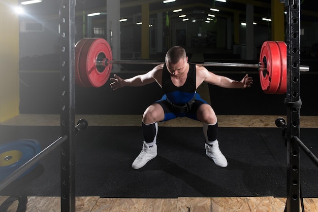 Photo powerlifter using barbell exercising legs inside gym