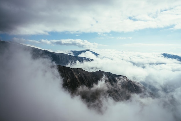 Prachtig alpenlandschap met grote rotsen en bergen in dichte lage wolken. Sfeervol hooglandlandschap met bergtoppen boven wolken. Prachtig uitzicht om bergtoppen te sneeuwen over dikke wolken.