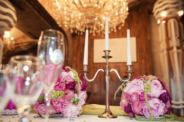 Prachtig bloemstuk aan de trouwtafel En kandelaar voor drie kaarsen op de achtergrond van kroonluchters