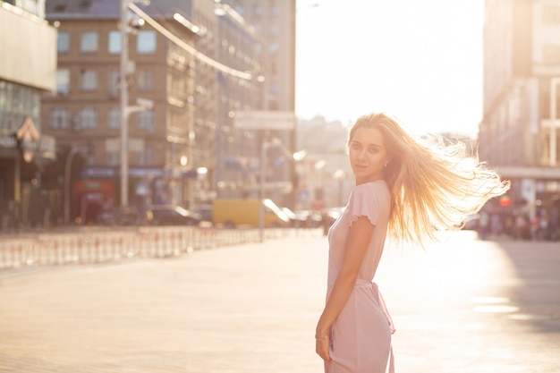 Prachtig blond model met wapperende haren die zich voordeed op de avenue in een zonnestralen. Ruimte voor tekst