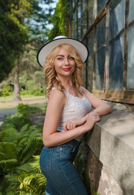 Prachtig jong model met hoed en stijlvolle outfit poseren in de buurt van de kas