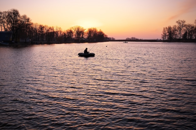 Prachtig landschap met oranje zonsopgang, meer en vissers in boten