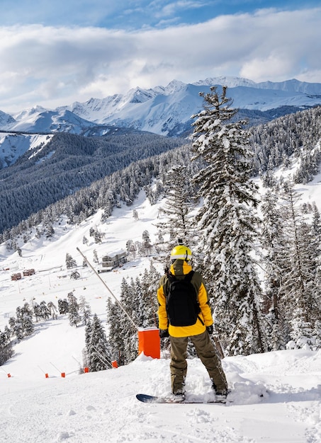 Prachtig landschap van het skigebied Arkhyz met bergen sneeuw bos en man snowboarder in gele jas en rugzak op een zonnige winterdag Kaukasus-gebergte Rusland