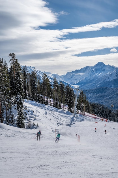 Prachtig landschap van het skigebied Arkhyz met bergen sneeuw bos skiërs en snowboarders op een zonnige winterdag Kaukasus gebergte Rusland verticaal