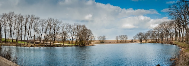 Prachtig landschap, vroege lente op een meertje, panorama. Weerspiegeling van riet, lucht en bomen in het water
