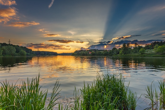 Prachtig meer omgeven door gras, bossen en kleurrijke gouden zonsondergang