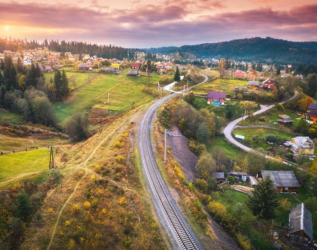 Prachtig oud treinstation en dorp bij zonsondergang in de Karpaten in de herfst in Oekraïne Luchtfoto van spoorweg groene weiden bomen huizen heuvels en kleurrijke rode lucht in de herfst Bovenaanzicht