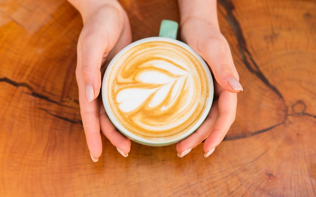 Prachtig patroonhart gemaakt door microfoam. Coffeeshop en café concept. Cappuccino van vrouwelijke handen. Ontwerp op het oppervlak van latte. Uitdaging voor latte artiest. Bovenaanzicht koffiekopje op houten tafel.