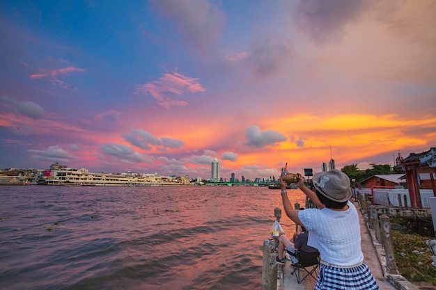 Prachtig uitzicht in de rode avondlucht van een vrouw die de chao phraya-rivier fotografeert