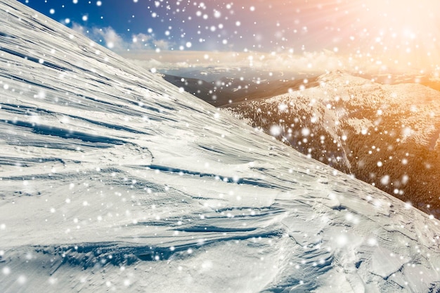 Prachtig winterlandschap Steile bergheuvelhelling met witte diepe sneeuw verre bergketen panorama grote sneeuwvlokken en helder stralende zonnestralen op blauwe hemel kleurrijke kopie ruimte achtergrond