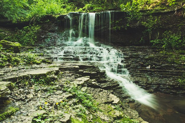 Prachtige berg regenwoud waterval met snel stromend water en rotsen lange blootstelling Natuurlijke seizoensgebonden reizen buiten achtergrond in hipster vintage stijl