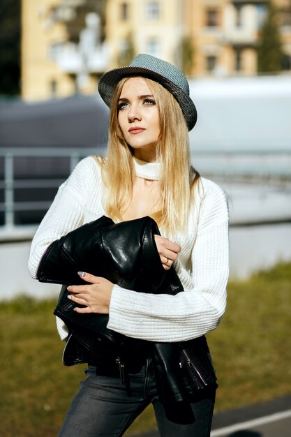 Prachtige blonde vrouw met hoed en gebreide trui, poseren in zonnige dag