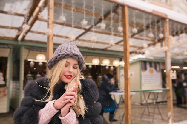 Prachtige blonde vrouw met smaakvolle kerst peperkoek tegen lichte decoratie op de kerstmarkt in Kiev