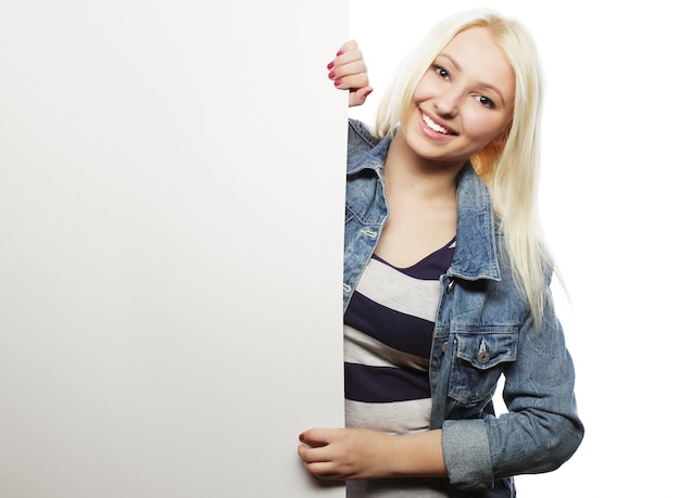 Prachtige blonde vrouw wijzend op een bord terwijl ze tegen een witte achtergrond staat