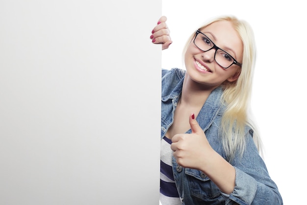 Prachtige blonde vrouw wijzend op een bord terwijl ze tegen een witte achtergrond staat