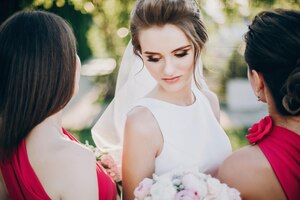 Prachtige bruid poseren met bruidsmeisjes in roze jurken met stijlvolle boeketten in warm avondlicht in zomerpark mooie gelukkige bruid met bruidsmeisje poseren samen