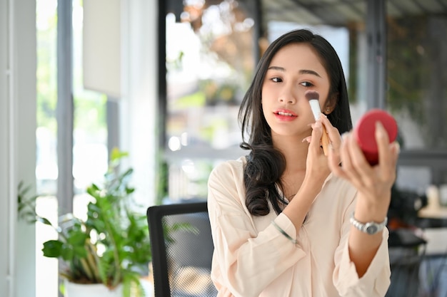 Prachtige duizendjarige Aziatische zakenvrouw die haar make-up opdoet in haar kantoor