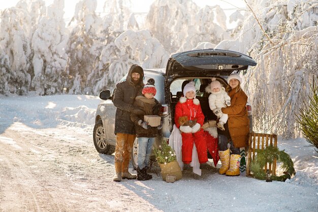 Prachtige familie staat naast de kofferbak van een suv in het winterbos, kerst vieren