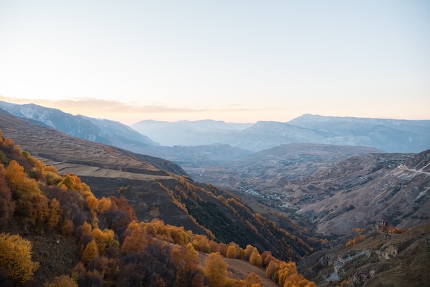 Prachtige grote vallei met oude bergen bedekt met herfstbos en groene velden onder heldere hemel in avondpanorama