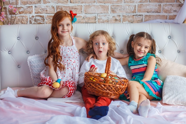 Prachtige kinderen zitten samen op een bed met paaseieren in hun handen en hebben plezier.