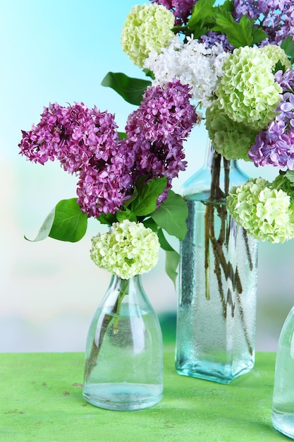 Prachtige lentebloemen in glazen flessen op houten tafel op lichte achtergrond